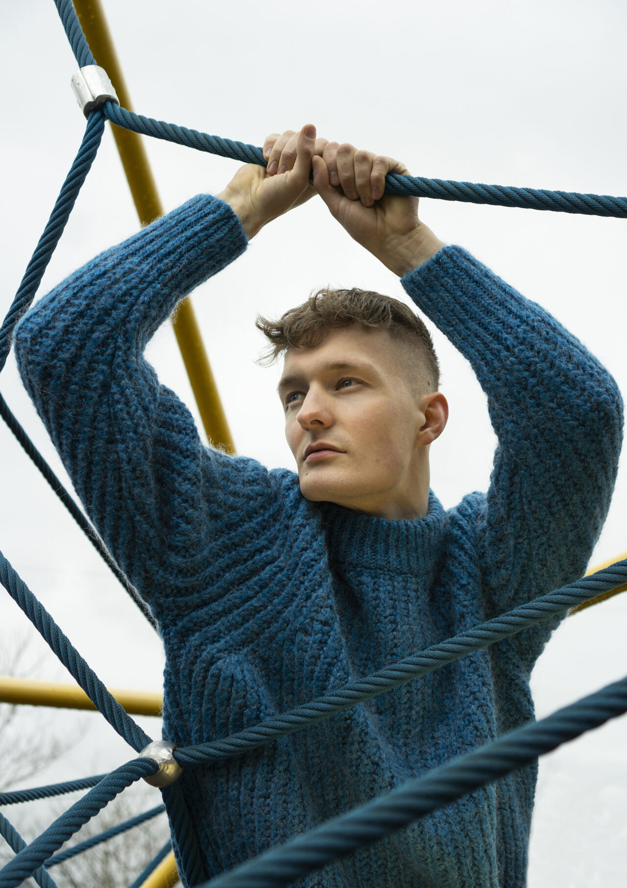 man standing in a kids playground, he is wearing a winter sweater